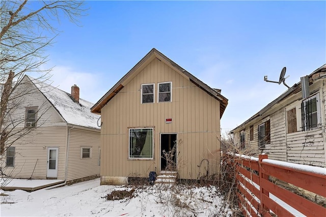 snow covered rear of property featuring entry steps and fence