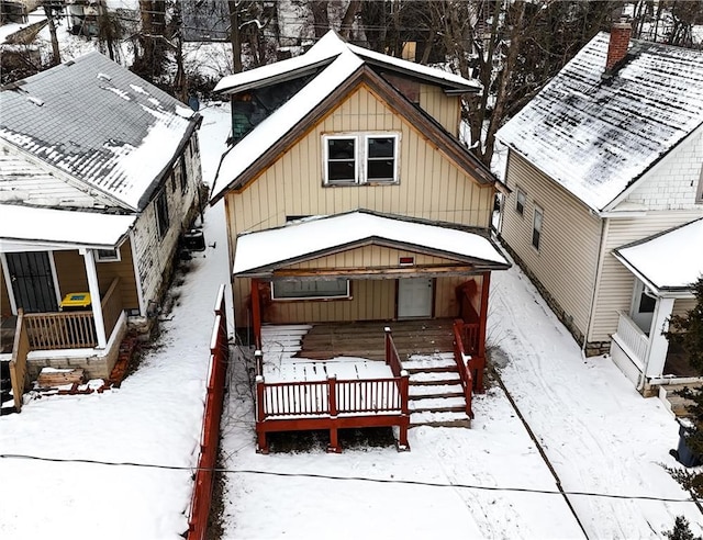 snow covered back of property with covered porch and board and batten siding