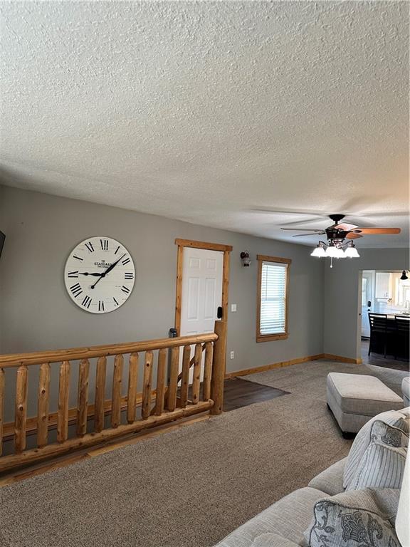 carpeted living room with a ceiling fan, a textured ceiling, and baseboards