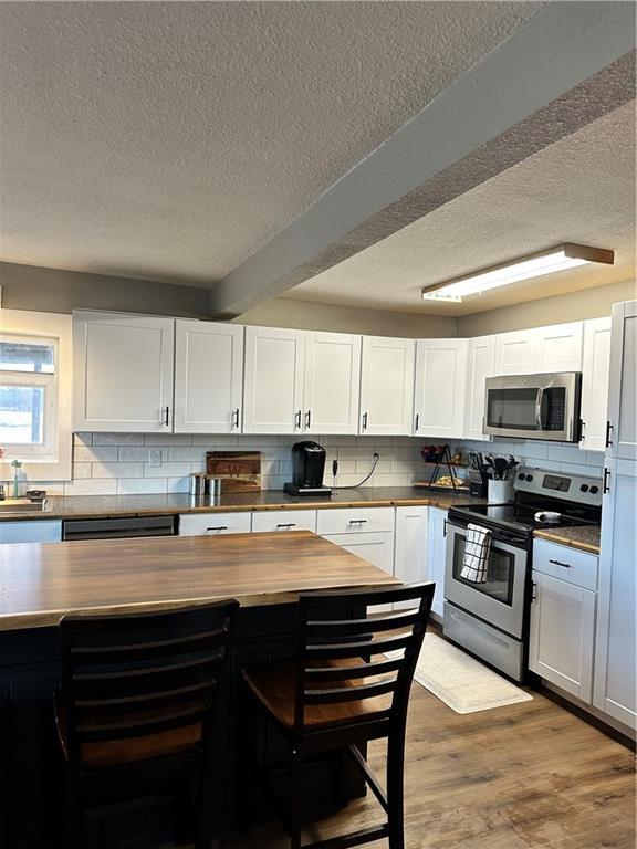 kitchen with butcher block countertops, white cabinetry, appliances with stainless steel finishes, light wood-type flooring, and decorative backsplash