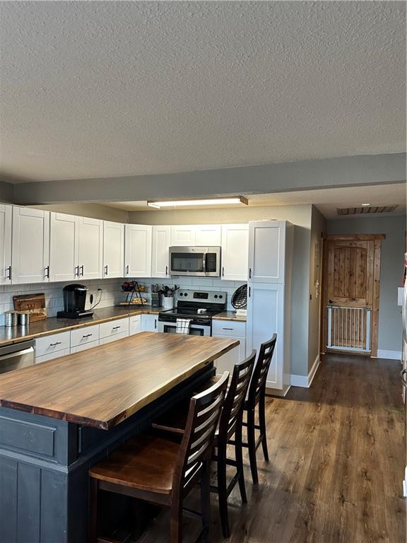 kitchen featuring wooden counters, backsplash, white cabinetry, and stainless steel appliances