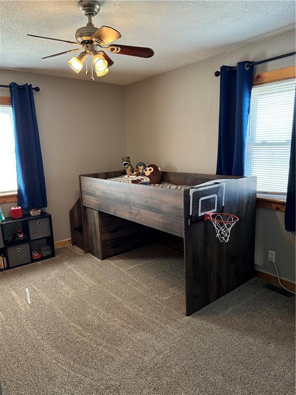 unfurnished bedroom featuring ceiling fan, multiple windows, carpet, and a textured ceiling