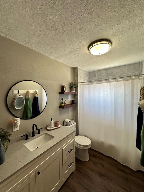 bathroom with curtained shower, toilet, vanity, a textured ceiling, and wood finished floors