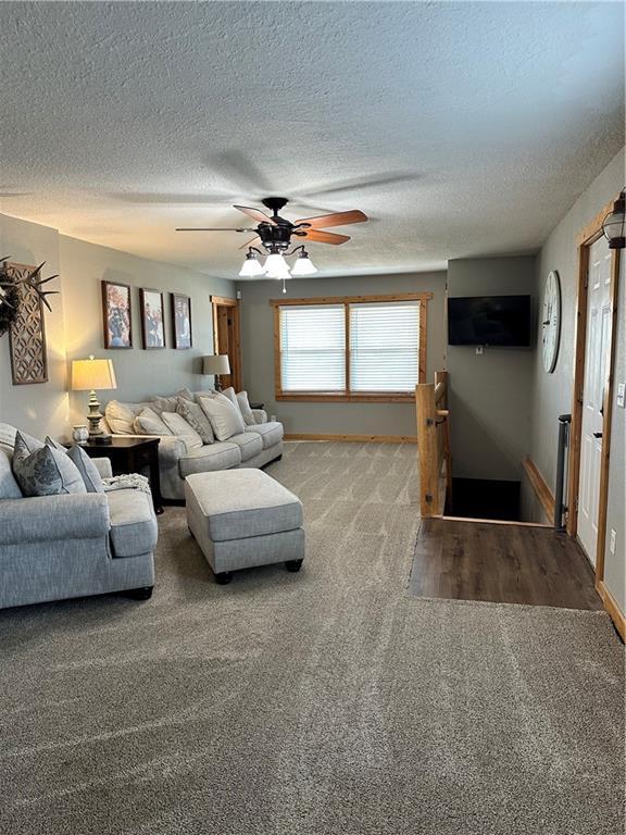 carpeted living area with a ceiling fan, a textured ceiling, and baseboards