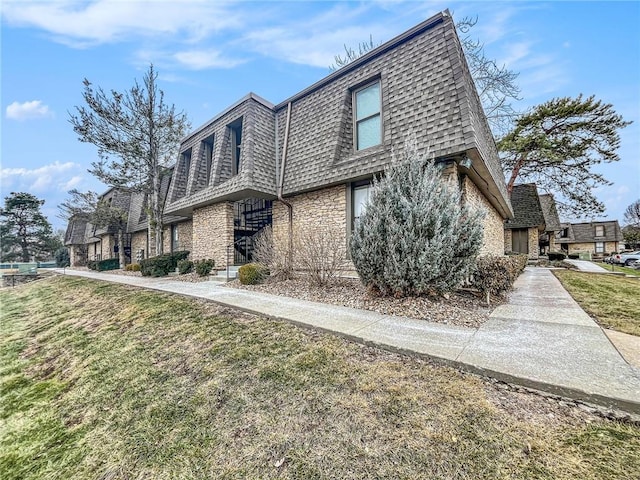 view of home's exterior featuring stone siding, roof with shingles, mansard roof, and a yard