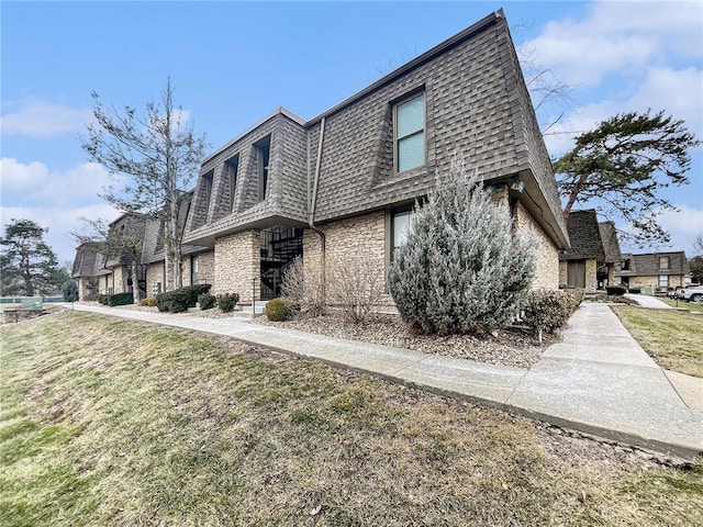 view of property exterior with stone siding, roof with shingles, a yard, and mansard roof