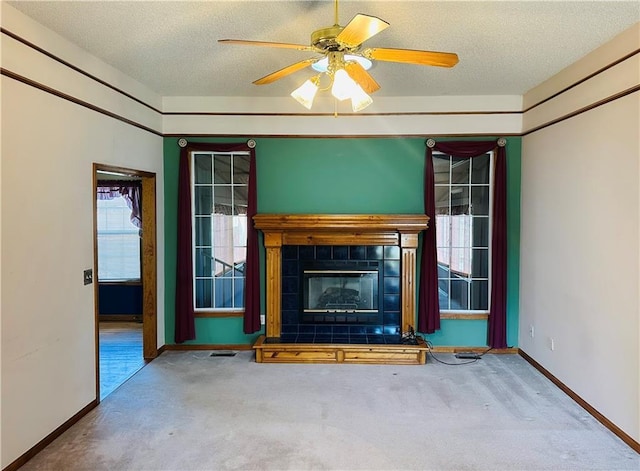 unfurnished living room featuring a wealth of natural light, a tile fireplace, a textured ceiling, and carpet