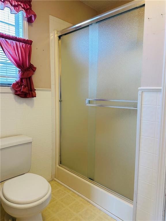 bathroom featuring tile walls, a shower with shower door, and toilet