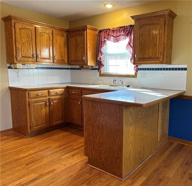 kitchen with sink, decorative backsplash, light hardwood / wood-style flooring, and kitchen peninsula