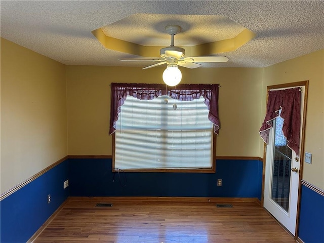 spare room with ceiling fan, wood-type flooring, a tray ceiling, and a textured ceiling