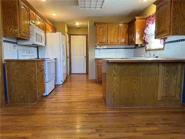 kitchen featuring white appliances, kitchen peninsula, decorative backsplash, and light wood-type flooring