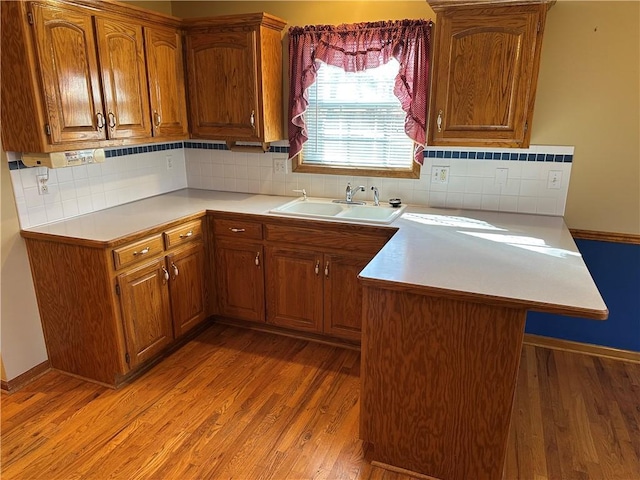 kitchen with tasteful backsplash, sink, light hardwood / wood-style floors, and kitchen peninsula