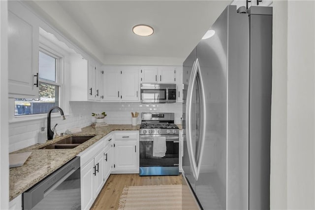 kitchen with light wood finished floors, stainless steel appliances, white cabinetry, a sink, and light stone countertops