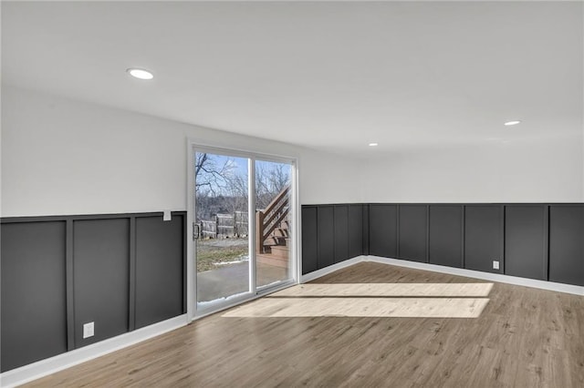 unfurnished room with a decorative wall, wainscoting, wood finished floors, and recessed lighting