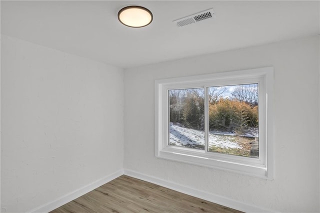 empty room with wood finished floors, visible vents, and baseboards