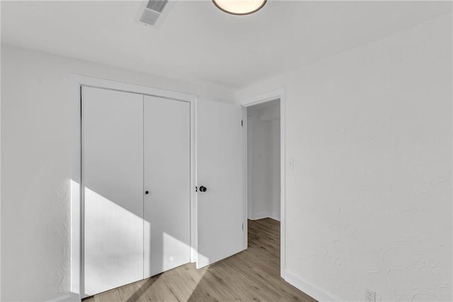 unfurnished bedroom featuring a closet, visible vents, baseboards, and wood finished floors