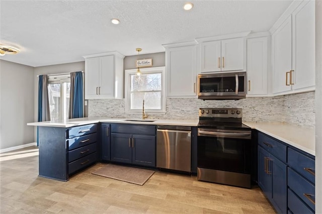 kitchen featuring a peninsula, a sink, white cabinets, blue cabinetry, and appliances with stainless steel finishes