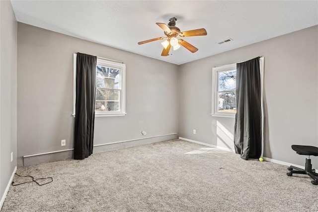 empty room with ceiling fan, carpet floors, visible vents, and baseboards