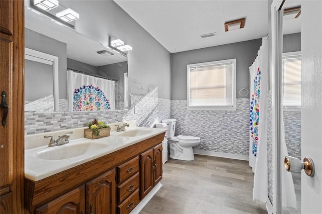 full bath with toilet, double vanity, visible vents, and a sink