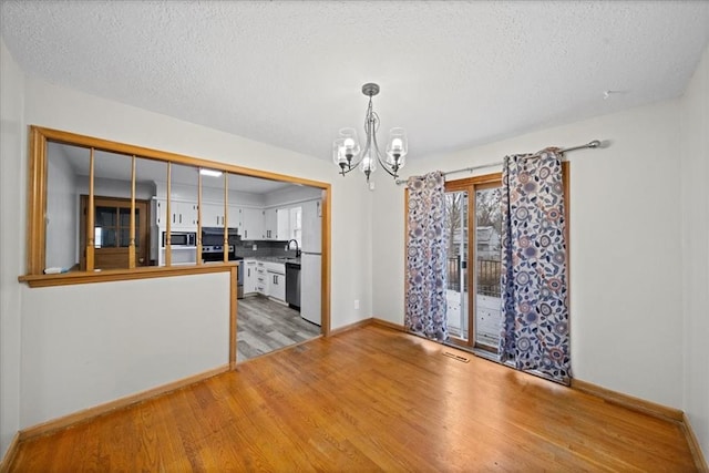 unfurnished dining area with light hardwood / wood-style floors, an inviting chandelier, sink, and a textured ceiling