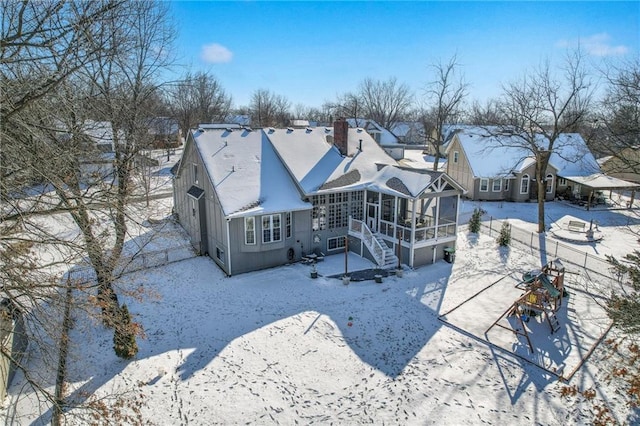 snow covered rear of property featuring a chimney, a sunroom, a garage, a residential view, and stairs