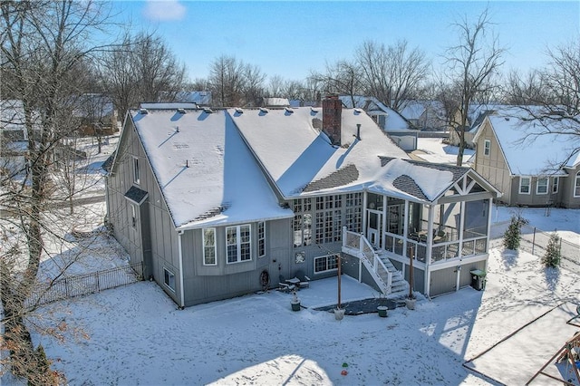 snow covered back of property featuring a garage, a sunroom, stairs, a residential view, and a chimney