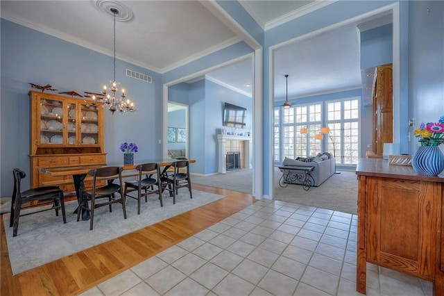 dining area with light tile patterned flooring, a notable chandelier, visible vents, ornamental molding, and a tiled fireplace