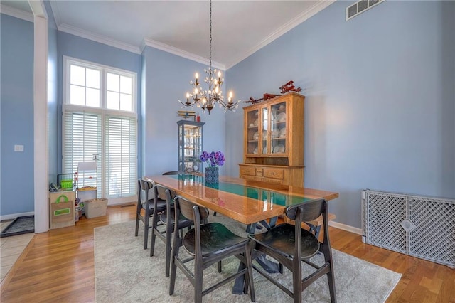 dining room featuring baseboards, light wood-style flooring, visible vents, and crown molding