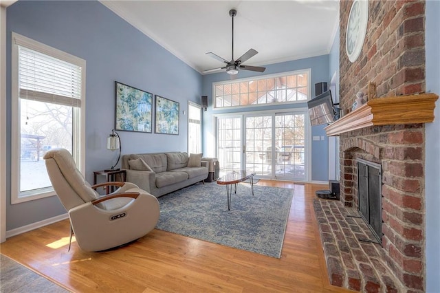 living room with crown molding, a fireplace, ceiling fan, wood finished floors, and baseboards