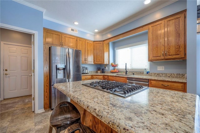 kitchen with brown cabinetry, light stone counters, stainless steel appliances, a kitchen bar, and a sink