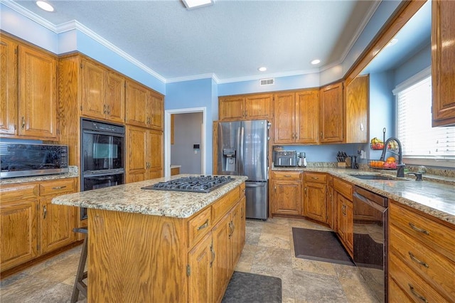 kitchen with visible vents, brown cabinetry, a kitchen island, appliances with stainless steel finishes, and a sink