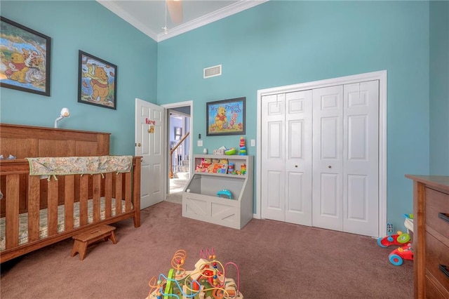 carpeted bedroom with a towering ceiling, ornamental molding, a closet, and a crib