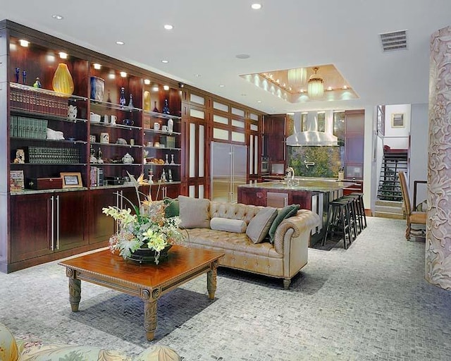 living room with a raised ceiling, ornamental molding, sink, and light colored carpet