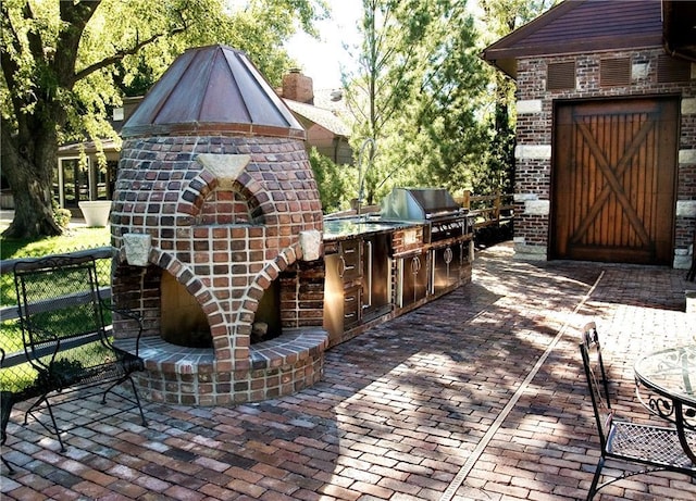 view of patio with an outdoor brick fireplace, an outdoor kitchen, and a grill