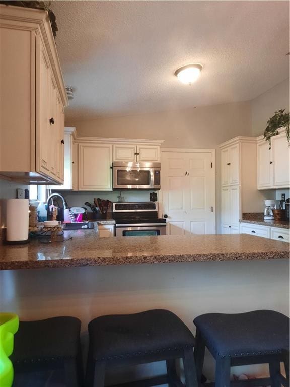 kitchen featuring sink, a kitchen breakfast bar, kitchen peninsula, stainless steel appliances, and a textured ceiling