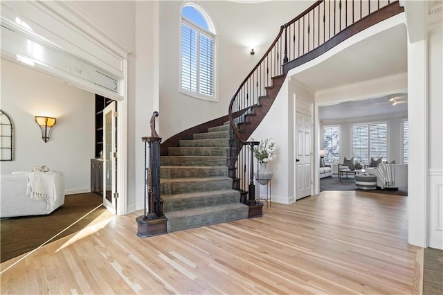 foyer entrance with ornamental molding, wood finished floors, a towering ceiling, and a healthy amount of sunlight