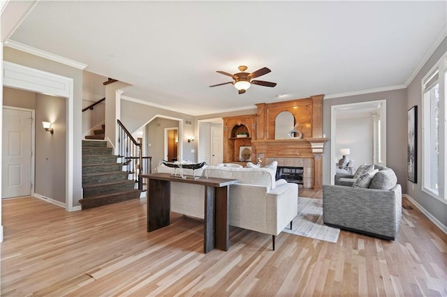 living room with ornamental molding, a fireplace, light wood finished floors, and stairs