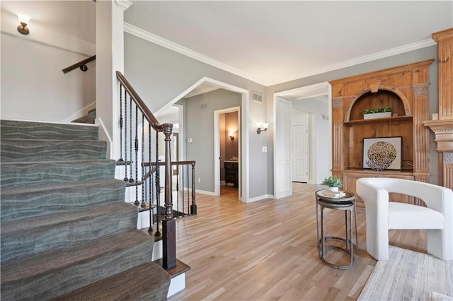 staircase with visible vents, crown molding, baseboards, and wood finished floors