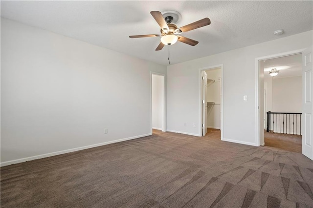 unfurnished bedroom with carpet floors, a walk in closet, a closet, a ceiling fan, and baseboards