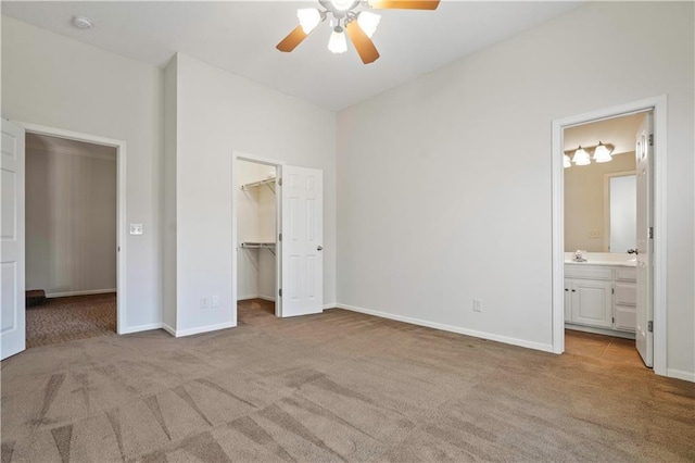 unfurnished bedroom with baseboards, light colored carpet, ensuite bath, a spacious closet, and a closet