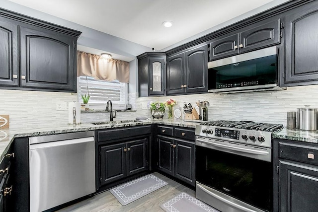 kitchen with sink, tasteful backsplash, appliances with stainless steel finishes, light stone countertops, and light hardwood / wood-style floors