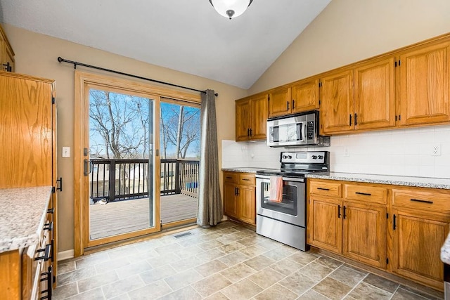 kitchen featuring visible vents, brown cabinets, backsplash, stainless steel appliances, and vaulted ceiling