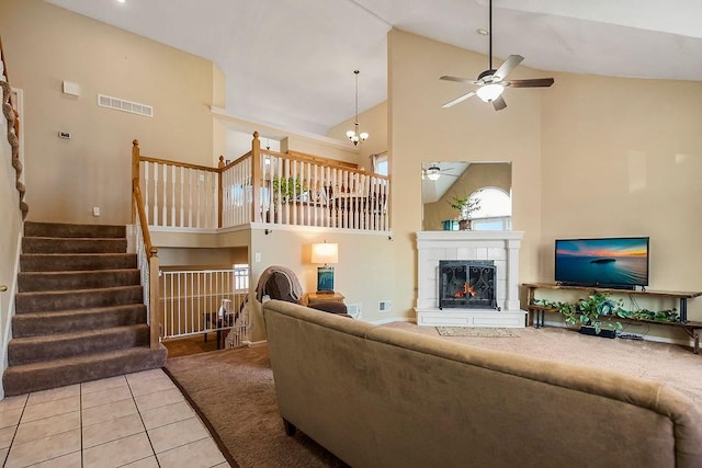 carpeted living room featuring visible vents, high vaulted ceiling, a tiled fireplace, ceiling fan with notable chandelier, and stairs