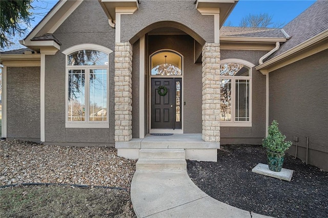 view of exterior entry featuring stucco siding and a shingled roof