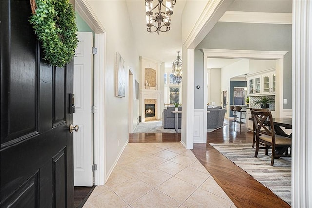 entryway with a glass covered fireplace, a chandelier, crown molding, and light tile patterned floors