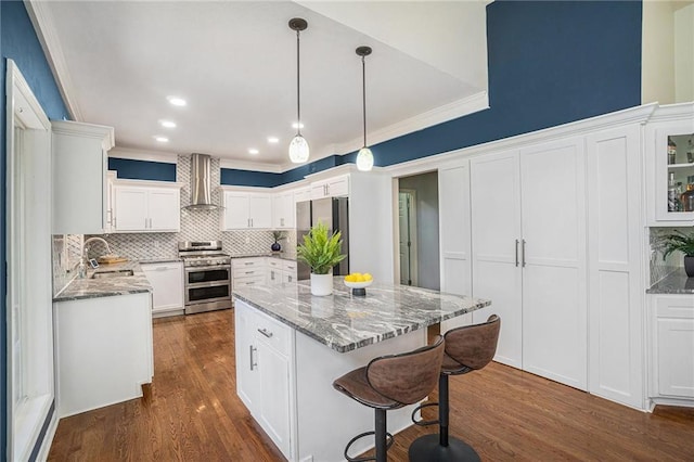 kitchen featuring wall chimney exhaust hood, light stone countertops, tasteful backsplash, and appliances with stainless steel finishes