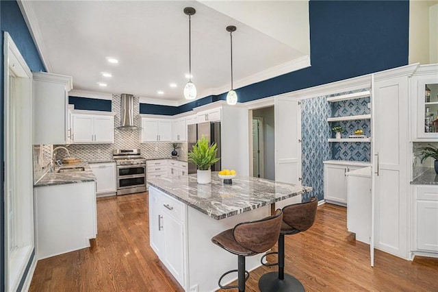 kitchen with light stone counters, white cabinets, appliances with stainless steel finishes, and wall chimney range hood