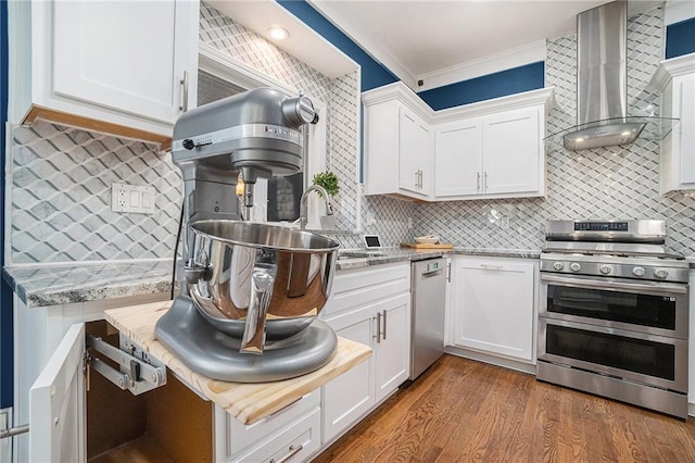 kitchen with tasteful backsplash, wall chimney range hood, ornamental molding, white cabinets, and stainless steel appliances