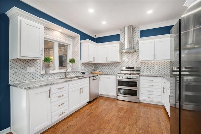 kitchen featuring a sink, light wood-style floors, appliances with stainless steel finishes, wall chimney exhaust hood, and light stone countertops