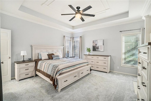 bedroom featuring light carpet, multiple windows, baseboards, and a tray ceiling